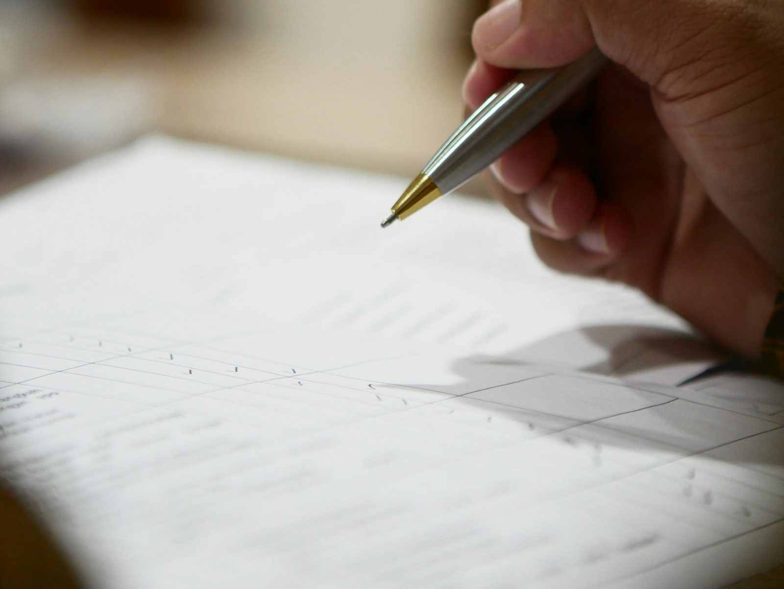 A hand signing a document with a silver pen